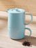 A light blue tea infuser set stacked together, featuring a teapot with a lid and a matching cup, alongside loose tea leaves.