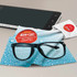 A screen cleaner cloth with water droplets in blue, alongside a pair of black glasses and a smartphone.