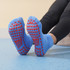 A pair of blue low cut kids' socks with red gripper dots on the soles, laid out against a light background.