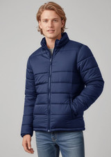 A man wearing a navy puffer jacket stands with a casual pose, featuring a zip-up front and pockets.
