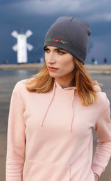 A grey beanie with a logo, worn by a woman in a pink hoodie, against a cloudy backdrop.