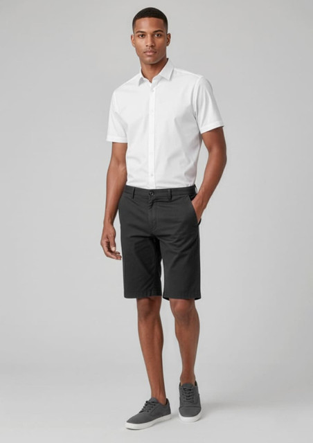 A man wearing black cargo shorts and a white short-sleeve shirt, paired with grey shoes, standing against a grey background.