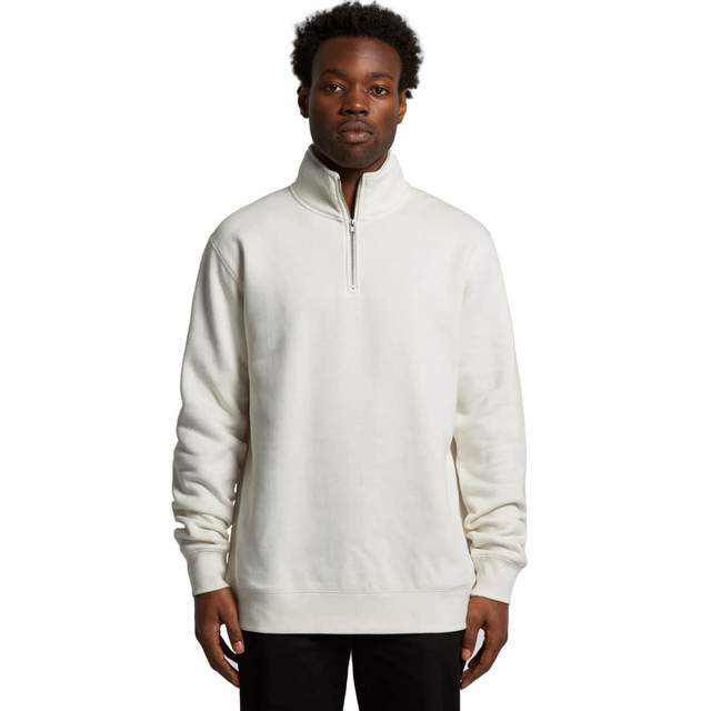 A man wearing a cream-coloured half zip crew jumper. The garment features a stand-up collar and has a logo.