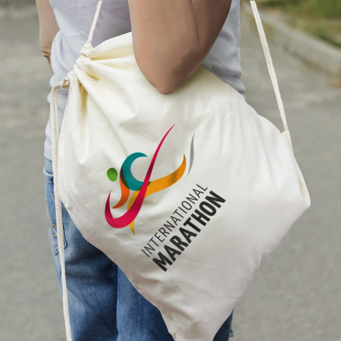 A cream cotton drawstring backpack is being carried, featuring a logo design and a colourful graphic.