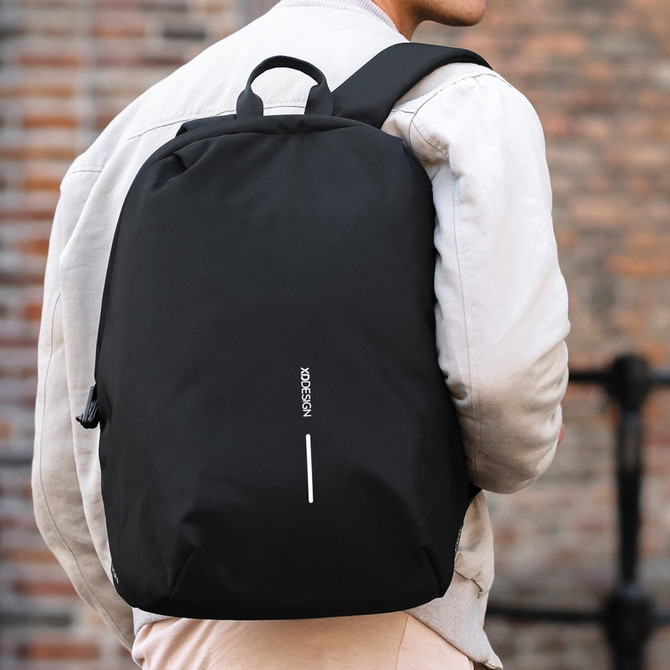 A black backpack with a logo, worn on the back of a person against a brick wall.