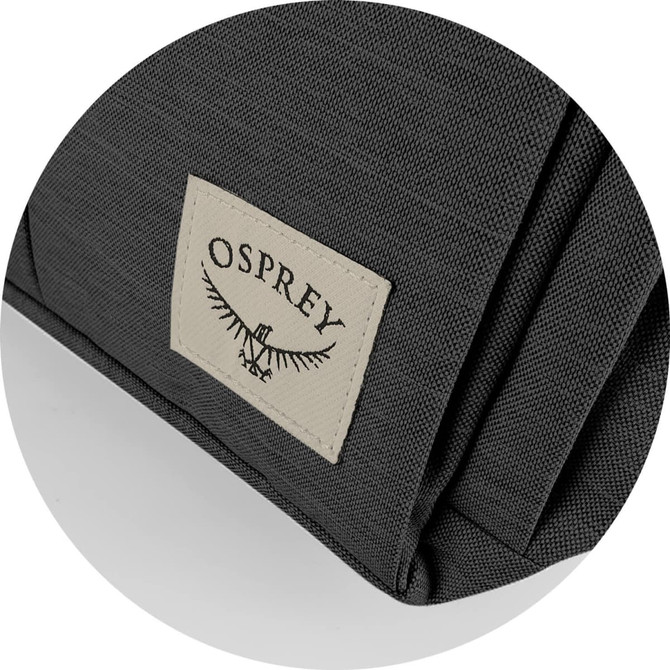 A close-up of a dark grey backpack fabric featuring an Osprey logo patch on the side.