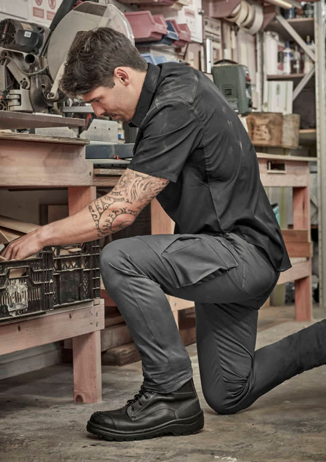 Men's essential basic stretch cargo pants in grey, featuring multiple pockets, worn by a man in a workshop setting.