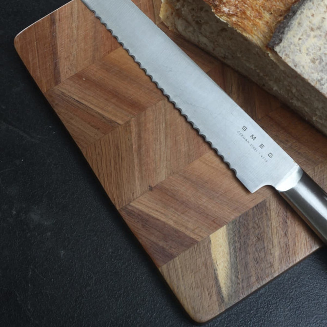 A wooden chopping board with a patterned design, featuring a stainless steel knife and a loaf of bread.