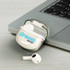A pair of white Bluetooth earbuds in a charging case, placed next to a laptop on a grey surface.