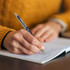 A metal pen in blue being used to write in a notebook on a wooden table.