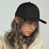 A black cap featuring a structured design and a curved brim, worn by a person with long, wavy hair.