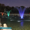 9-arch pond fountain illuminated with purple LED lighting at night, displaying a fan-shaped water spray pattern in a pond with stone edging and trees in the background.