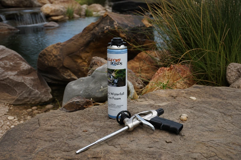 Half Off Ponds Black Waterfall Gun Foam can with foam gun applicator displayed on rock beside pond and waterfall