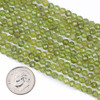 Cherry Tree Beads Peridot 4mm Faceted Round Beads shown next to a coin for size reference on a 15-inch strand of natural gemstone beads.