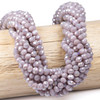 Crystal 5x6mm opaque light lavender purple faceted rondelle beads with AB finish displayed on a wooden rod for jewelry making.