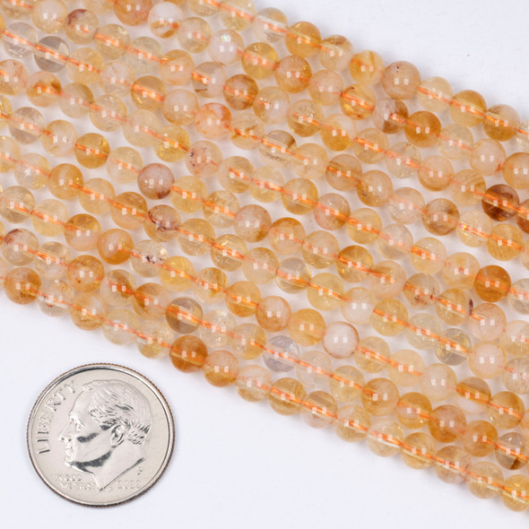 Cherry Tree Beads Citrine 4mm Round Beads shown next to a coin for size reference on a 15-inch strand of natural gemstone beads.