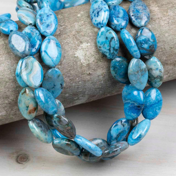 Strands of Special Gems dyed blue crazy lace agate marquise beads, approximately 10x15mm in size, made from gemstones and displayed wrapped around a textured wood log.
