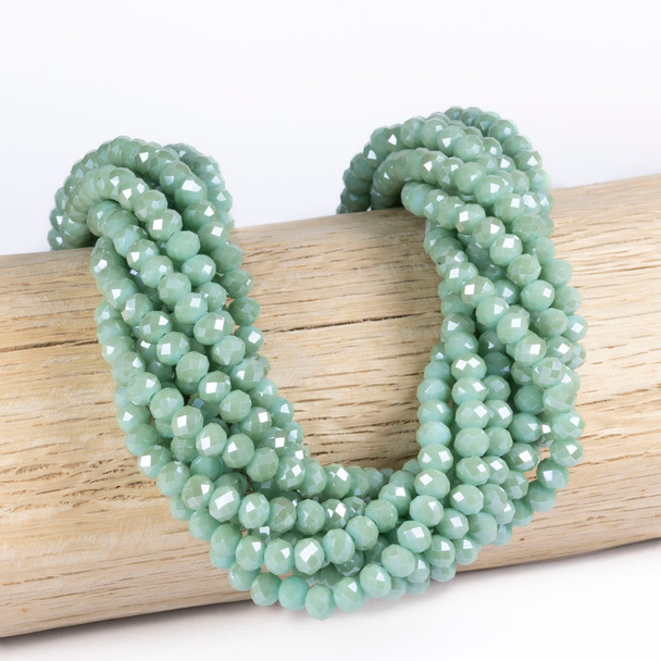 Cherry Tree Beads Crystal 5x6mm Faceted Rondelle, Opaque Eucalyptus Green beads draped on a wooden display, 15 inch strand for jewelry making.