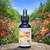 Bottle of Aunt Flo’s Secret Weapon flower essence placed on a stone in a sunlit garden filled with colorful flowers.