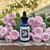 Raubritter Rose flower essence bottle on a cottage garden bench with sprays of pink roses around it.