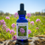 Bottle of Dames Rocket flower essence in a meadow with flowers blooming behind it. 