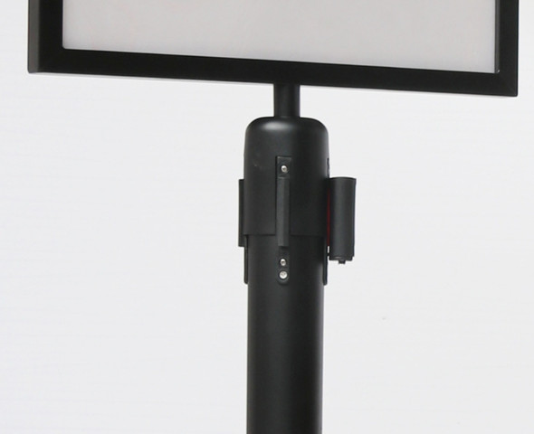 Black sign holder fitted to the top of a queue barrier post