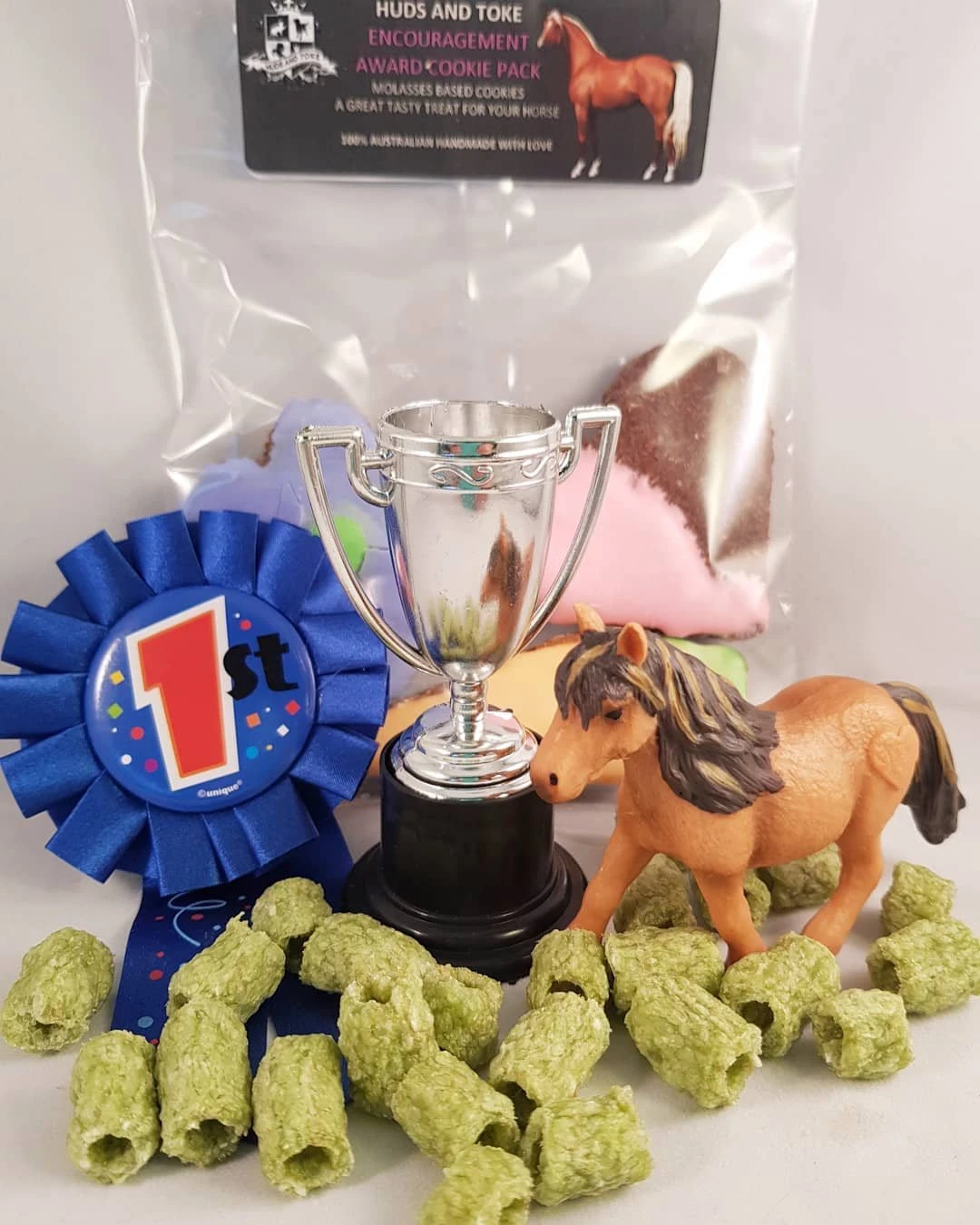 A Huds and Toke Encouragement Award pack with a blue first place rosette, a small trophy, a toy pony and green Horse Bix