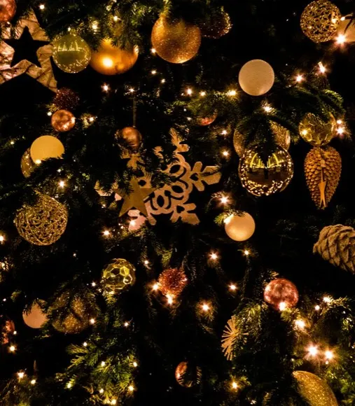 Gold baubles, finials and snowflake ornaments on a lit Christmas tree