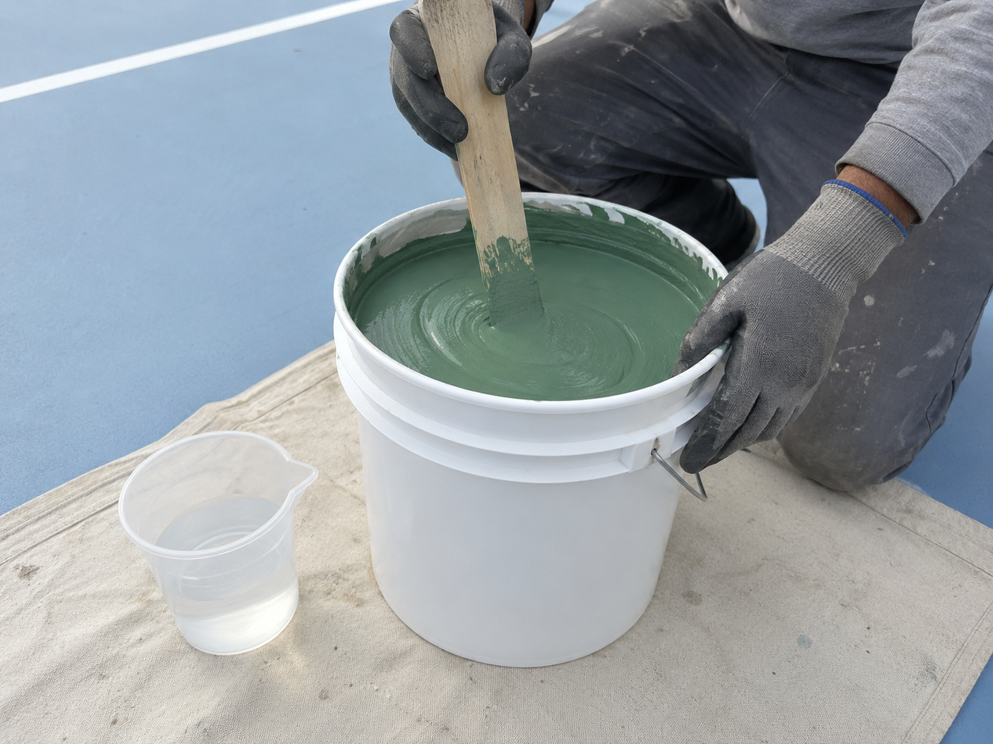 Contractor manually stirring Court Green acrylic coating after measuring clean water for thinning