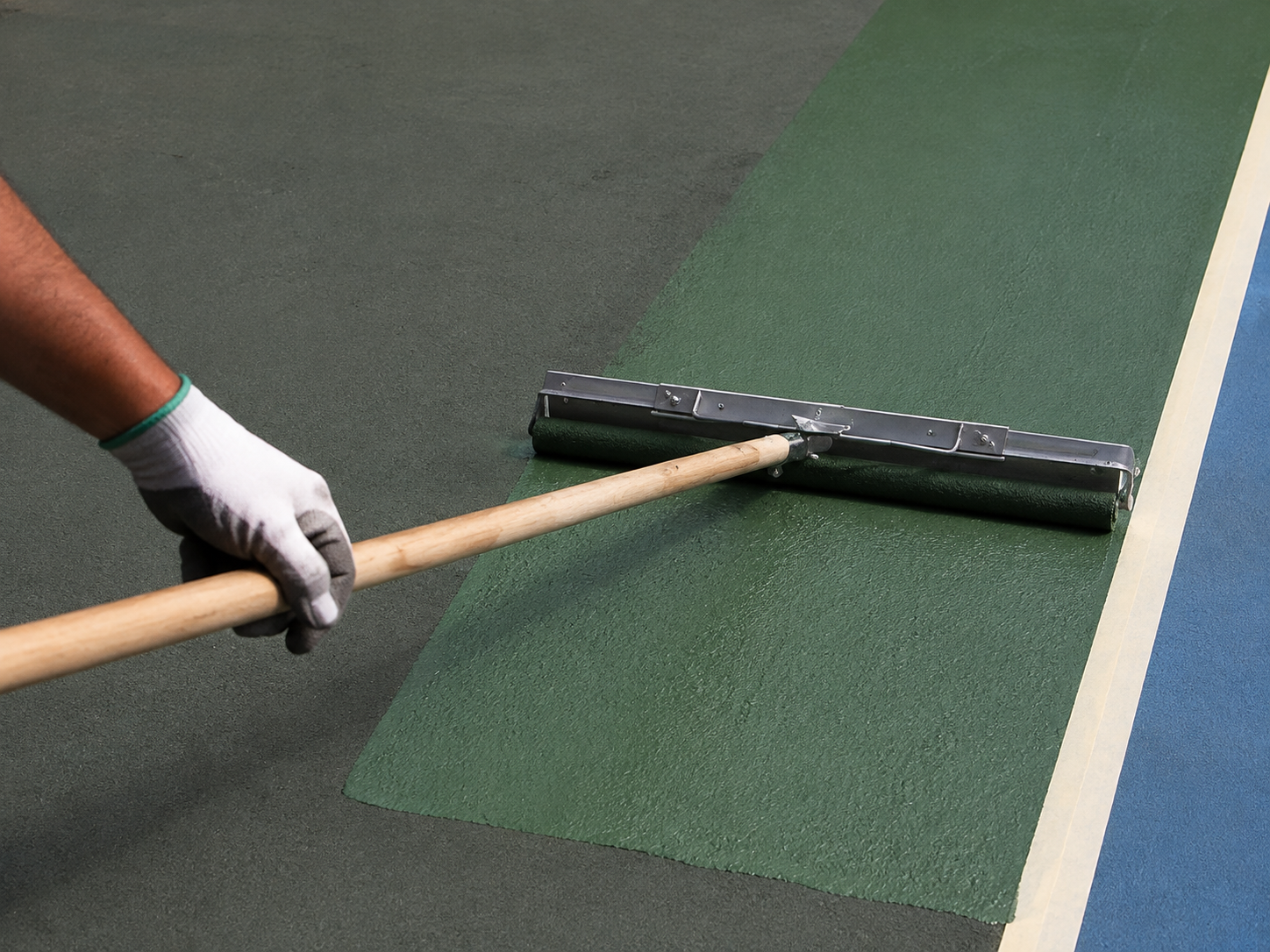 Contractor spreading Court Green acrylic coating with a wide low-profile court roller