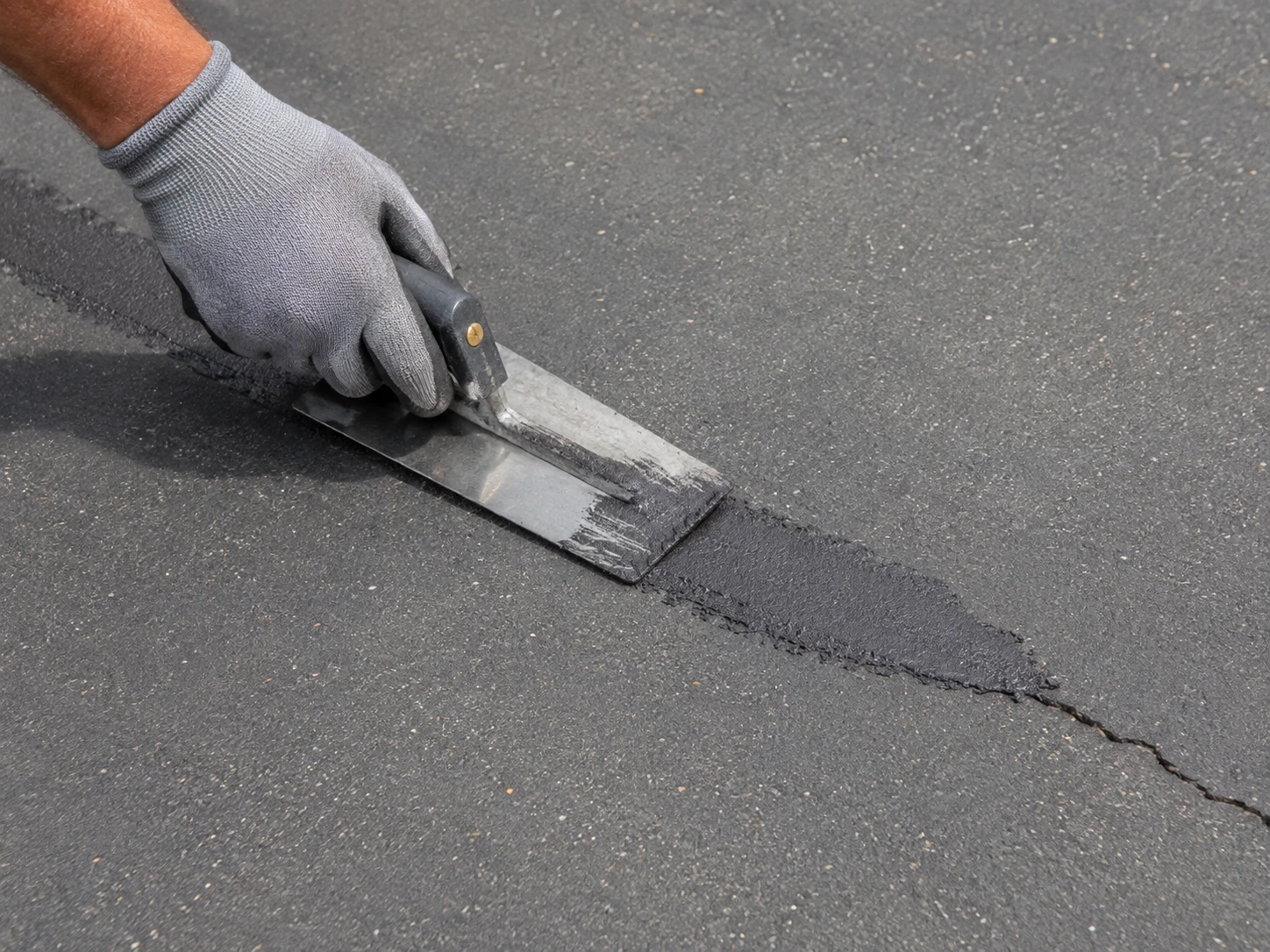 Contractor filling a crack in an asphalt court surface
