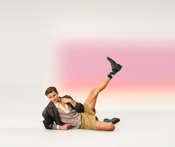 Model wearing luxury dress shoes styled with khaki shorts and a casual layered outfit.