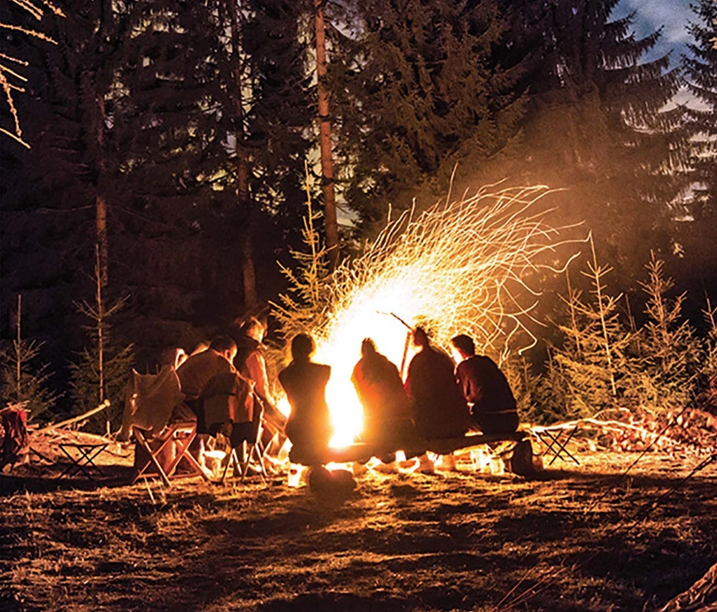 Friends gathered around a campfire in the woods at night