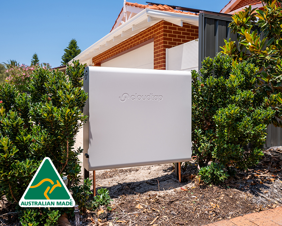 A Surf Mist Cloudtap Design Series system in front of a brick house, surrounded by green shrubery