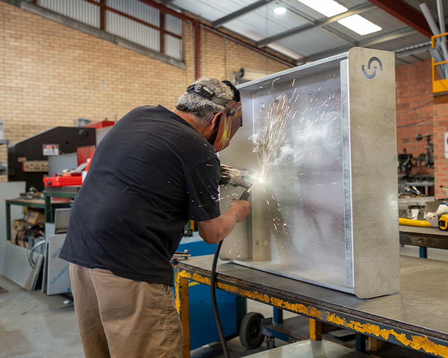 A worker in a protective helmet welding a Cloudtap Design Series frame on a table