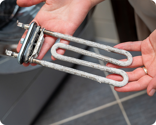 Hands holding a rusty, corroded washing machine heating element over a tiled floor