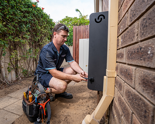 An installer crouches beside a house, installing a Scaleclear unit