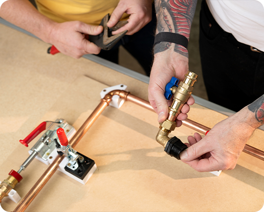 Two people assemble copper plumbing pipes on a workbench