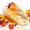 Thick fillet portion of Alaska halibut with halved tomatoes drizzled with sauce.