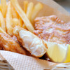 A basket of Pubhouse battered halibut fillets with fries & a lemon wedge.