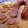 A partially sliced Alaska reindeer sausage link with cracker & cheese appetizers.
