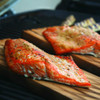 Copper River sockeye salmon fillets on cedar planks above a grill.