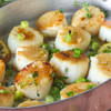 Caramelized Alaska scallops in cooking pan with diced scallions.