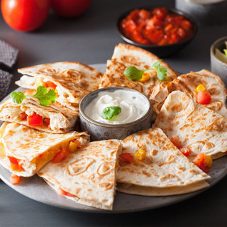 Warm shrimp quesadillas wedges arranged around a bowl of sour cream mix.