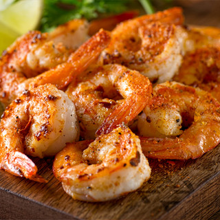 Freshly grilled seasoned shrimp on a dark-wood cutting board.