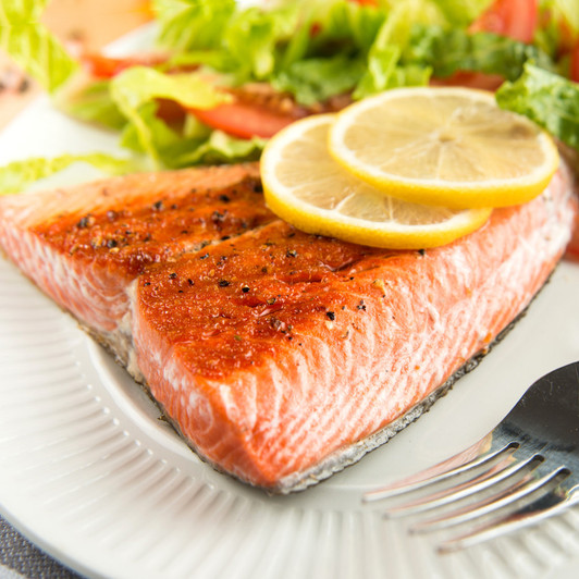 Just roasted, Alaska sockeye salmon tail portion with lemon slices and salad.