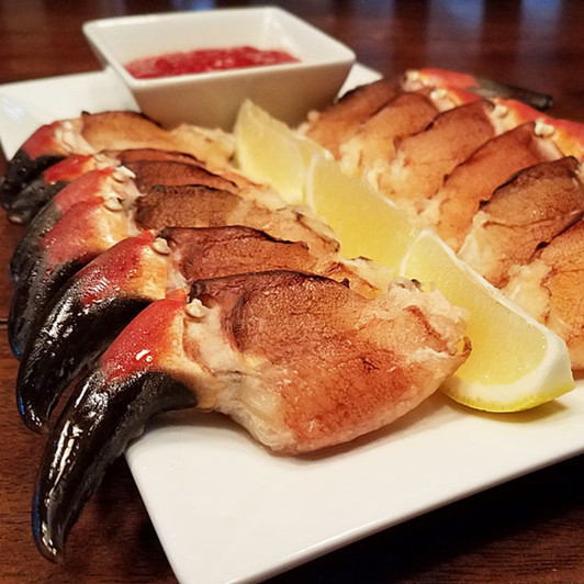 Rock crab cocktail claws arranged on a platter with dipping sauce & lemons.