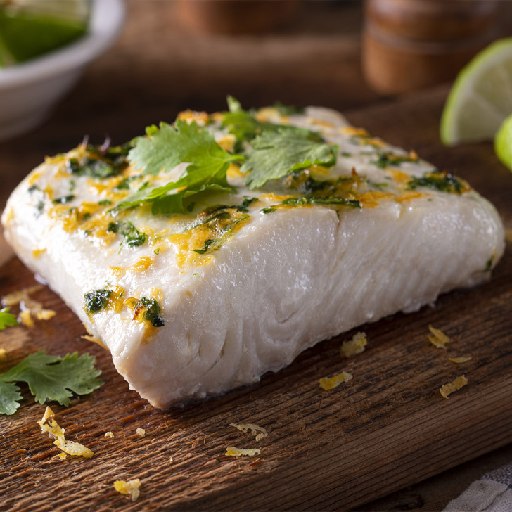 Moist halibut fillet portion on a cedar board with lime wedges.