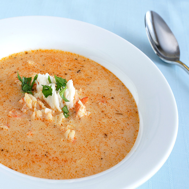 Creamy king crab bisque in a white ceramic shallow bowl, with chunks of king crab on top.