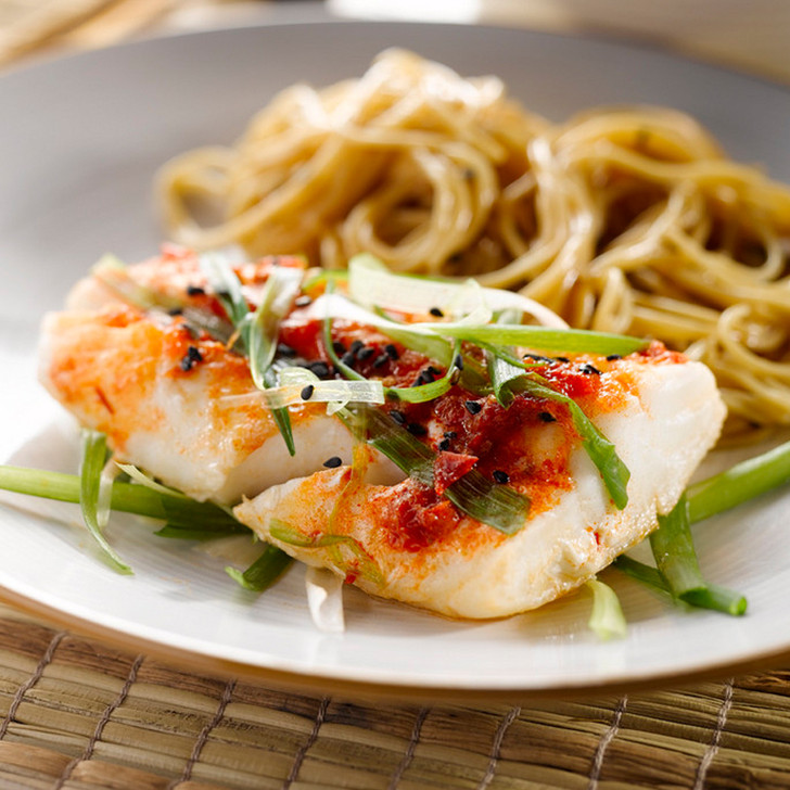 Cooked Alaska halibut tail portion on a plate with noodles.